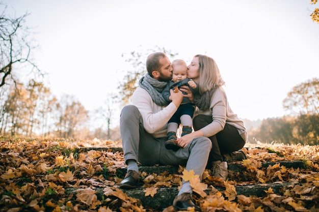De gelukkige zitting van het familiepaar op treden die door de herfstbladeren worden behandeld en hun mooi kind kussen.