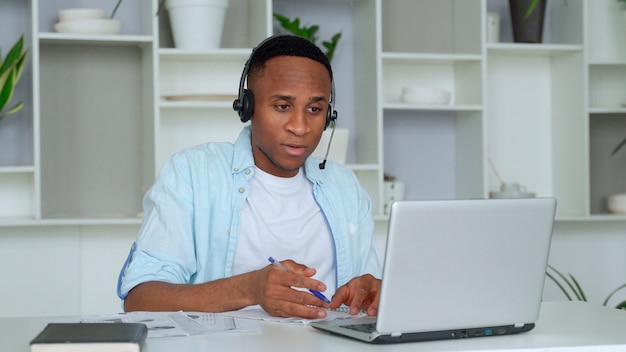 De gerichte zwarte adviseur met een hoofdtelefoon bekijkt laptop