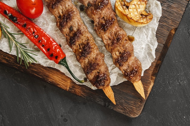 De geroosterde lula-kebab op vleespennen diende op houten raad, zwarte lijstachtergrond