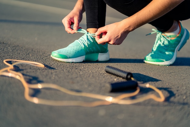 De geschiktheidsvrouw bindt schoenveters op tennisschoenen en treft voorbereidingen om in openlucht cardiooefeningen met touwtjespringen te doen
