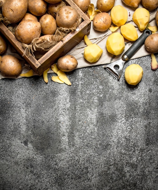 De geschilde aardappelen met een oude houten doos op rustieke tafel.