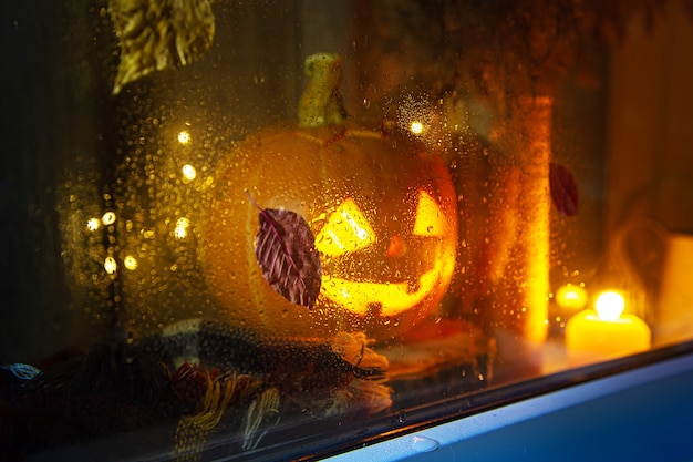 De gesneden pompoen kijkt uit het raam. Jack Lantaarn, Halloween-concept. Regenachtig, herfst. Focus op glas.