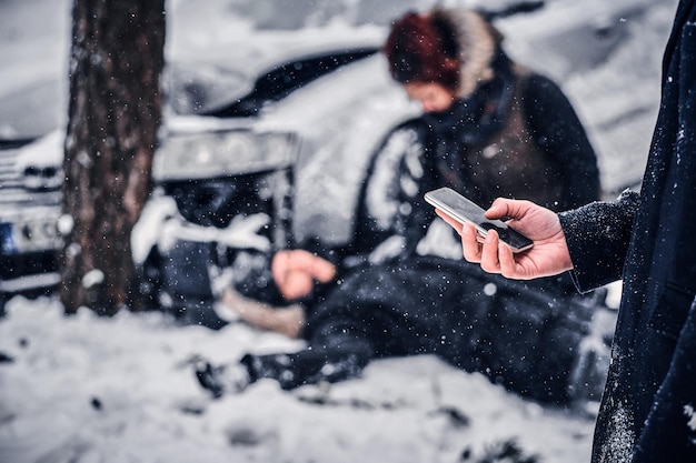 De getuige van het ongeval houdt de telefoon en gaat de reddingsdienst bellen. de auto kwam in een slip en crashte op een besneeuwde weg tegen een boom.