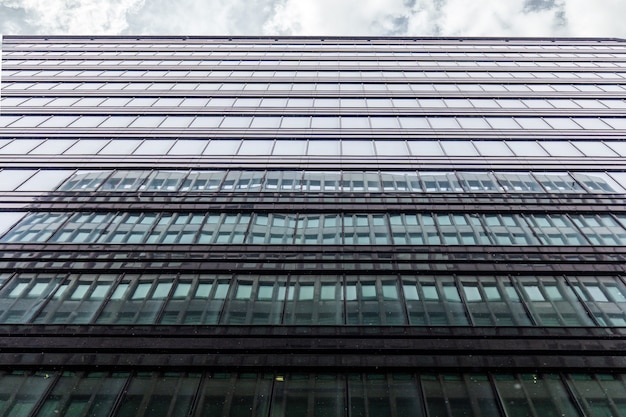 De gevel van het kantoorgebouw neergeschoten met een horizontale strook grijze lucht met wolken. De ramen van het zakencentrum weerspiegelen het aangrenzende gebouw