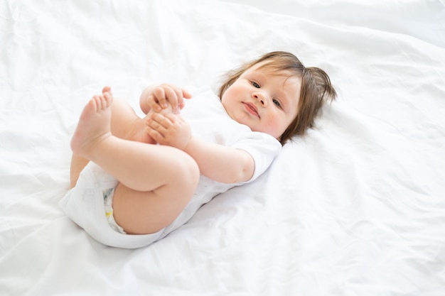 De gezonde jongen die van de 6 maandbaby en thuis op een wit beddegoed glimlacht ligt.