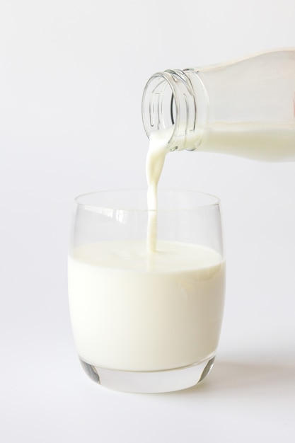 De gietende melk van de glasfles in een glas op witte achtergrond