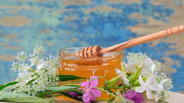 De glazen pot met verse honing op de rustieke achtergrond. Bloemen op tafel.