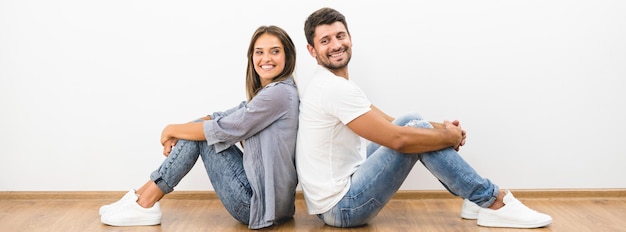 De glimlach man en vrouw zitten op de achtergrond van de lege muur