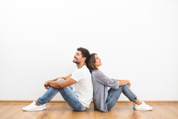 De glimlach man en vrouw zitten op de achtergrond van de lege muur