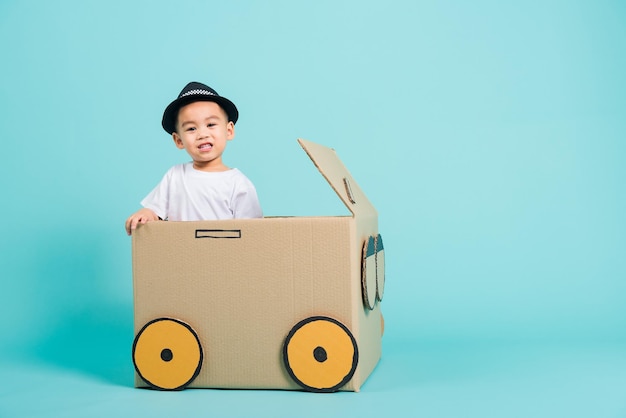 De glimlach van babykinderenjongen in het drijven van spelauto creatief door een kartondoos