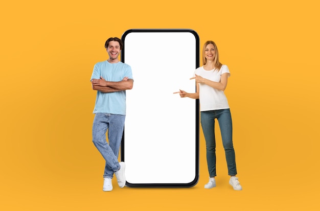 De glimlach van het jonge echtpaar is aanstekelijk terwijl ze naast elkaar staan en een grote smartphone met een