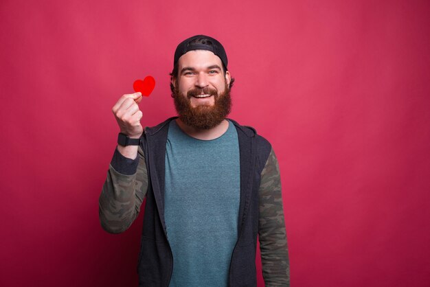 De glimlachende hipstermens houdt een rood klein hart