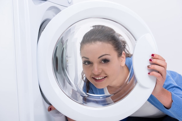 De glimlachende huisvrouw doet wasserij met wasmachine.