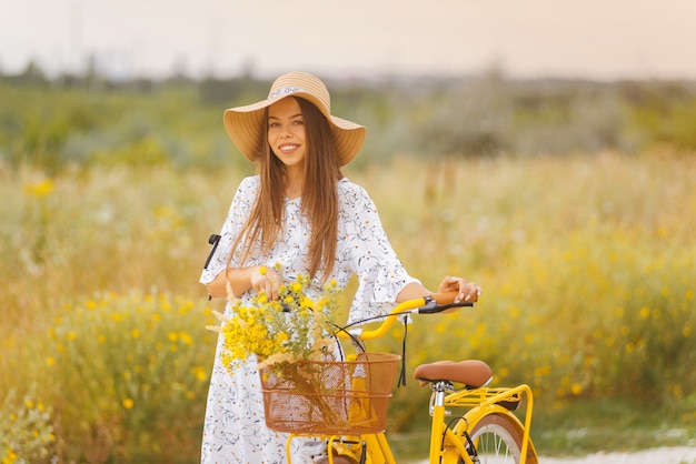 De glimlachende jonge dame loopt met haar fiets op een gebied van gele bloemen