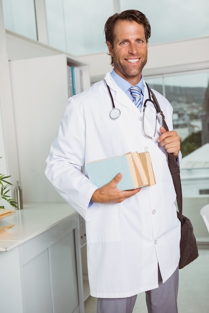 De glimlachende mannelijke boeken van de artsenholding in medisch bureau
