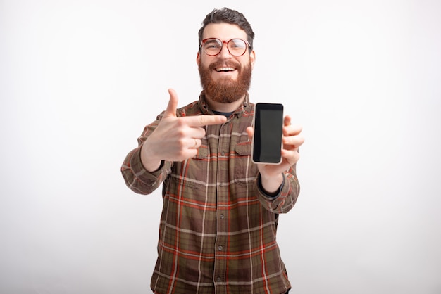 De glimlachende mens die glazen en baard dragen richt op zijn telefoon.