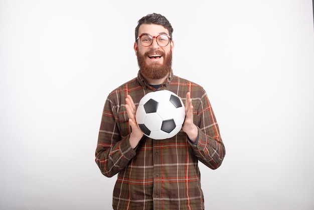 Foto de glimlachende mens is opgewekt omdat hij de voetbalbal op witte achtergrond heeft gevangen.