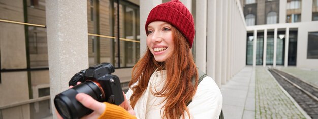 Foto de glimlachende roodharige meisjesfotograaf die foto's maakt in de stad, maakt foto's buitenshuis op professional