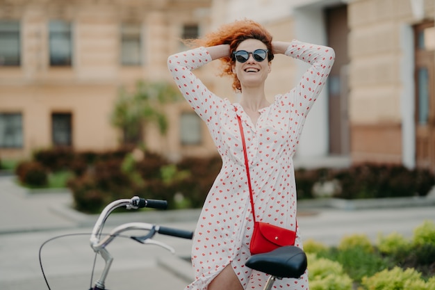 De glimlachende vrouw berijdt fiets in stad, houdt handen op hoofd achter