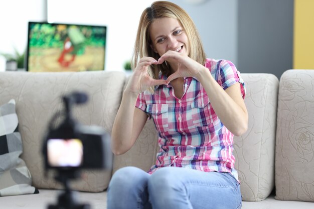 De glimlachende vrouw toont haar hart aan camera op statief