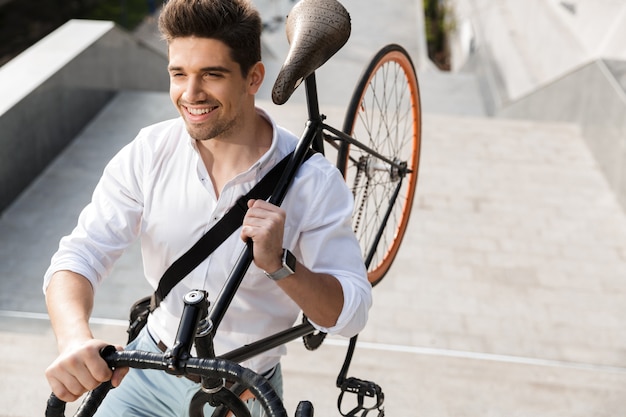 De glimlachende zakenman kleedde zich in overhemd dat een fiets draagt