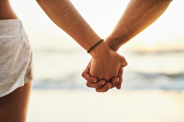 De golven komen en gaan, maar ik blijf voor altijd Bijgesneden opname van een jong stel dat elkaars hand vasthoudt op het strand