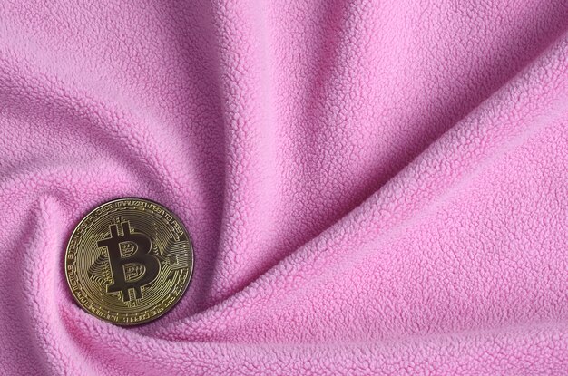 De gouden bitcoin ligt op een deken van zacht en donzig lichtroze fleece