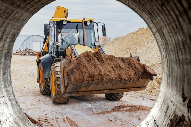 De graafmachine vult de put met de voorste bak Verplaatst grond rond de bouwplaats Close-up Zware bouwmachines