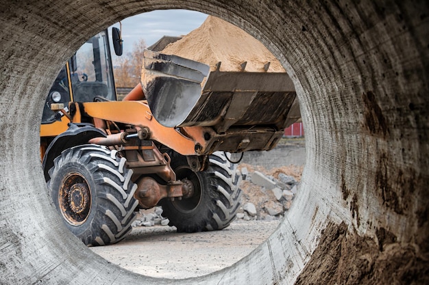 De graafmachine vult de put met de voorste bak Verplaatst grond rond de bouwplaats Close-up Zware bouwmachines