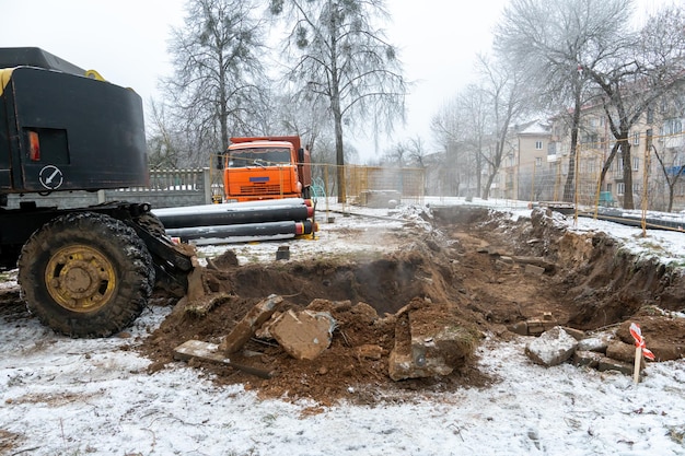 De graafmachine werkt op de bouwplaats om de pijpleiding in de winter te vervangen Gaten graven voor het leggen van nieuwe pijpen voor centrale verwarming in een woonwijk