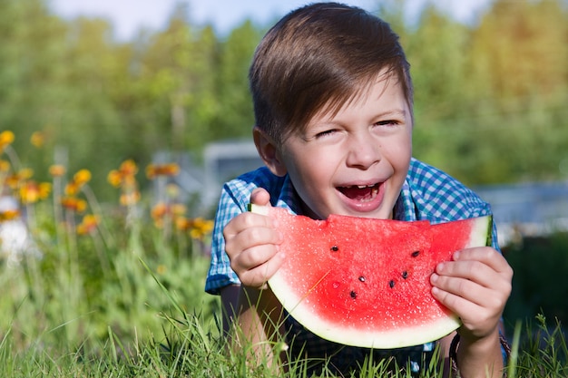 De grappige jongen eet in openlucht watermeloen in de zomerpark