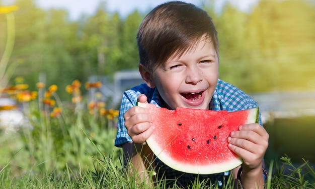 De grappige jongen eet in openlucht watermeloen in de zomerpark