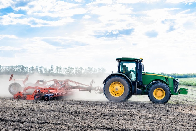 De groene tractor cultiveert het land in het veld Landbouwwerk