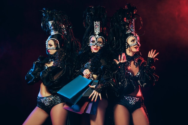 De groep jonge gelukkig lachende mooie danseressen met carnaval jurken poseren met boodschappentassen op zwarte studio achtergrond