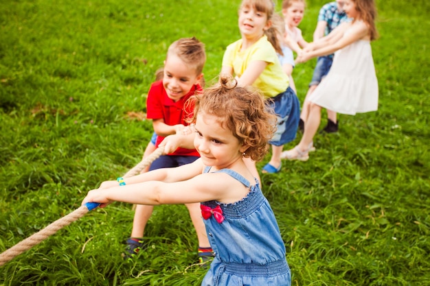 De groep kleine kleuters speelt touwtrekken op het gras De foto met focus op front girl