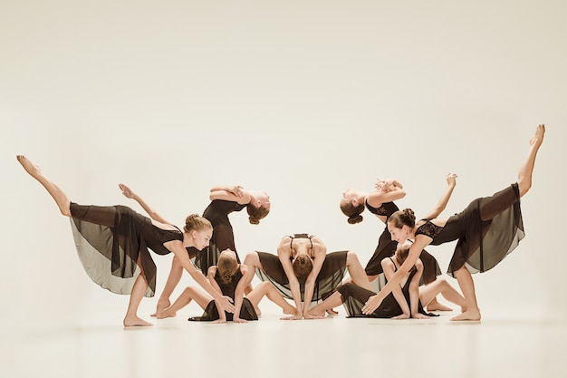 De groep moderne balletdansers die op grijze studioachtergrond dansen