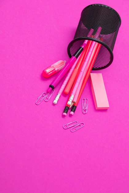 De groep roze producten van de kleurenkantoorbehoeften is verspreid van potloodbak van boven naar beneden op geïsoleerd roze