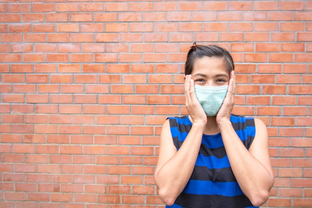 De hand die het masker op Aziatische van het vrouwengezicht bakstenen muur houdt als achtergrond.