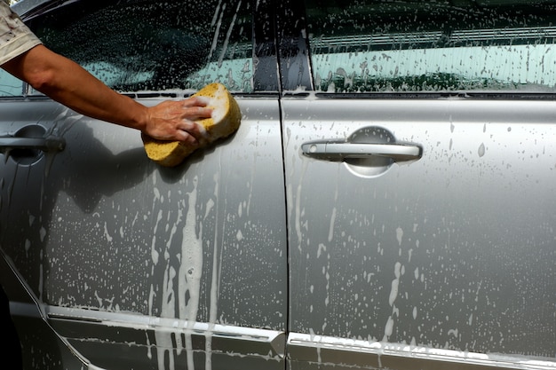 De hand die van de mens zijn zilveren auto thuis in het ochtendzonlicht wast