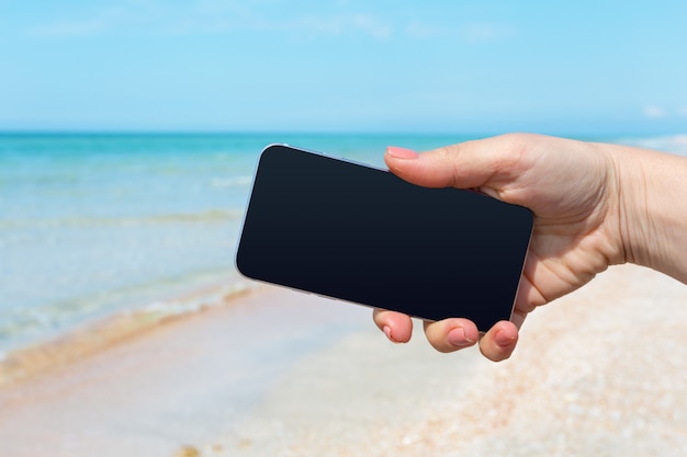 De hand die van de mooie vrouw slimme telefoon met behulp van bij strand