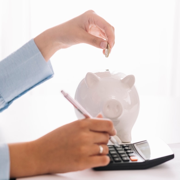 Foto de hand die van de vrouw calculator gebruikt terwijl het opnemen van muntstuk in piggybank