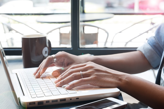 De hand die van de vrouw laptop computer in koffie met behulp van