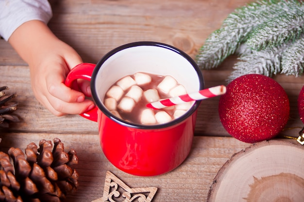 De hand die van het kind rode mok Kerstmiscacao op houten lijst houden