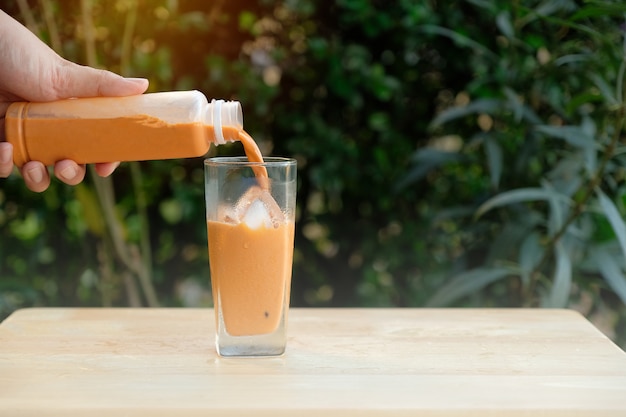 De hand giet koude Thaise thee uit een fles in het glas met ijs.