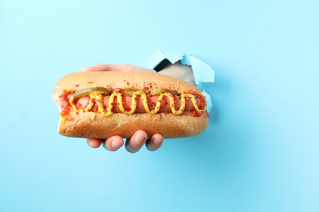 De hand houdt hotdog van gat op blauwe oppervlakte