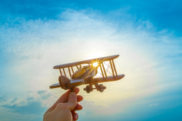 De hand met een houten vliegtuig op de achtergrond van de zonsondergang