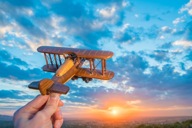 De hand met een speelgoedvliegtuig op de achtergrond van een zonsondergang