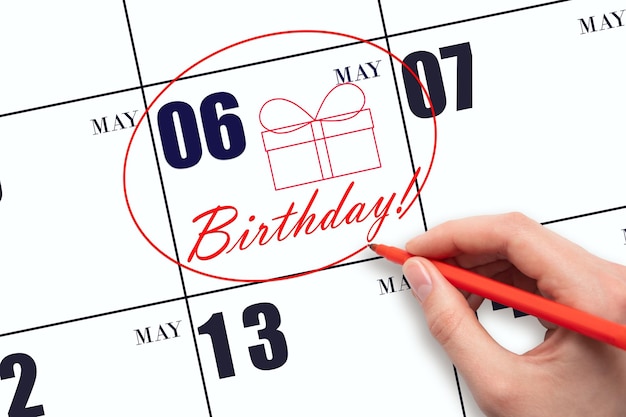 De hand omcirkelt de datum op de kalender 6 mei tekent een geschenkdoos en schrijft de tekst birthday holiday