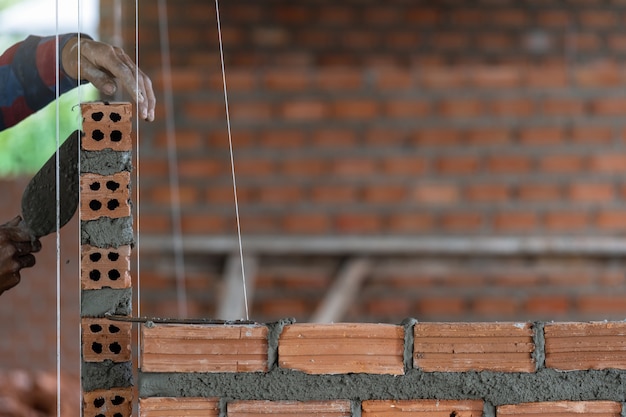 De hand professionele bouwvakker die van de close-up bakstenen in nieuwe industriële plaats legt