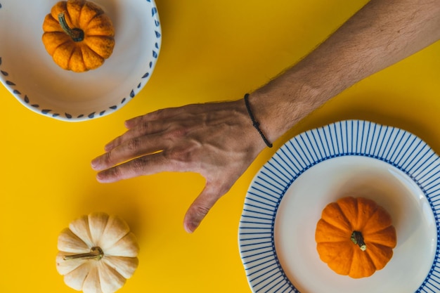 Foto de hand reikt naar een kleine pompoen tegen de achtergrond van de uitgespreide pompoenen op geel